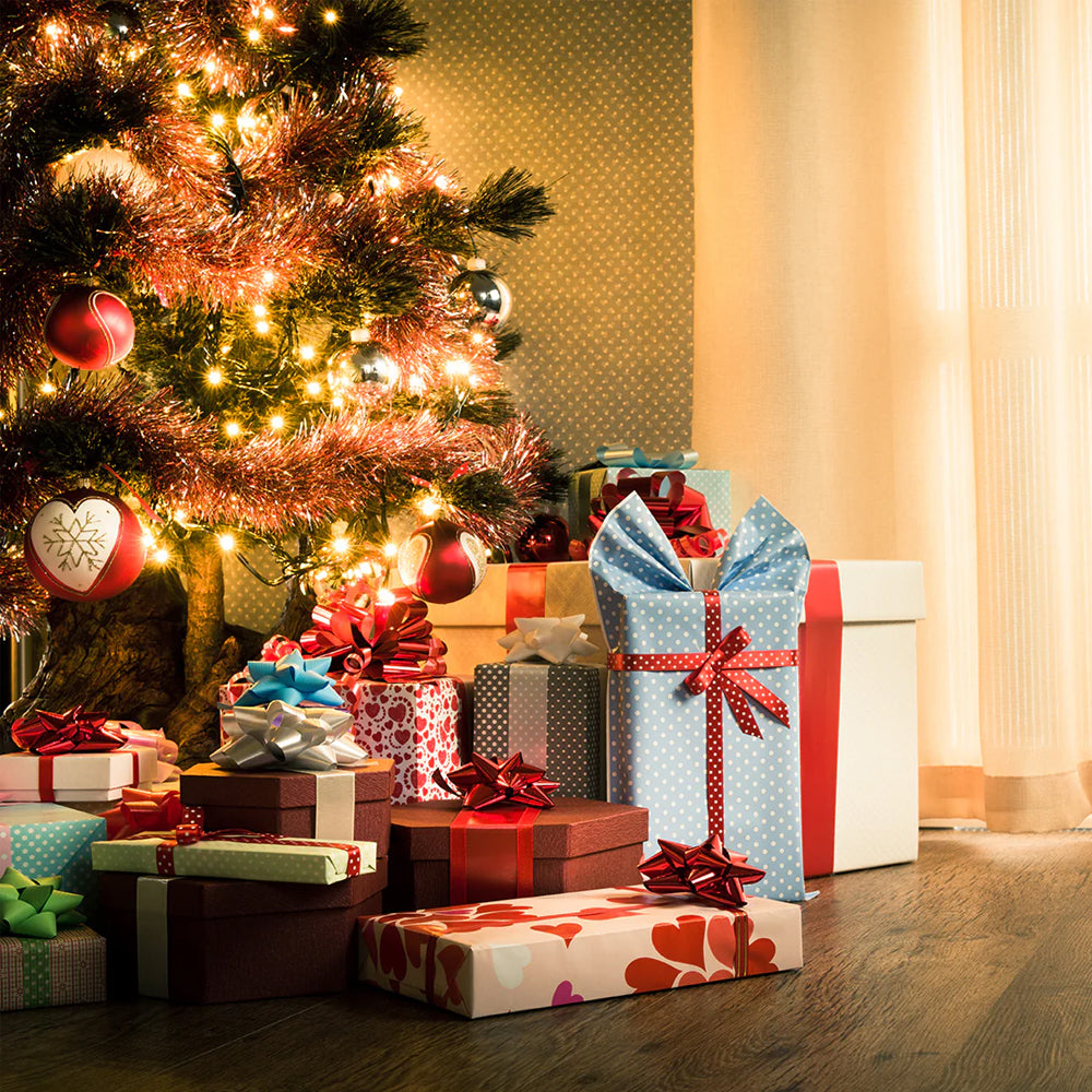 Beleuchteter Weihnachtsbaum mit Geschenken auf Holzfußboden vor hellem Vorhang.