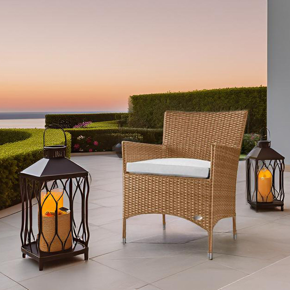 Naturfarbener Rattanstuhl mit weißem Kissen auf Terrasse bei Sonnenuntergang, flankiert von Laternen.