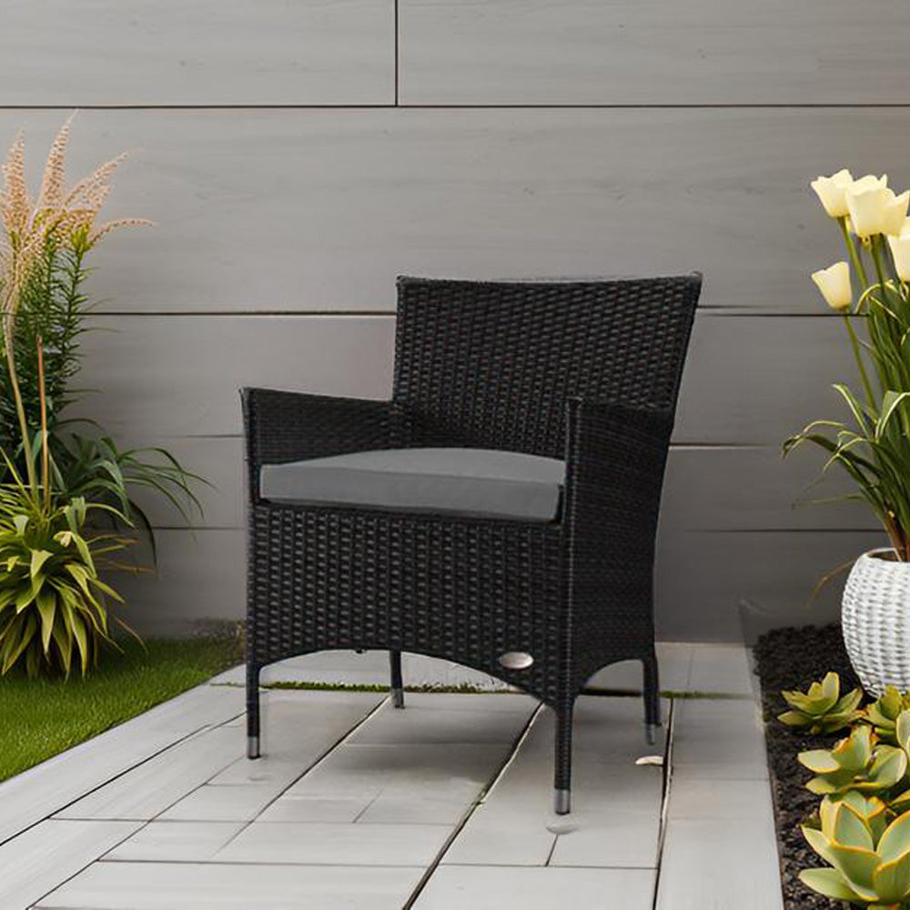 Schwarzer Rattanstuhl mit grauem Kissen steht auf moderner Terrasse, umgeben von Pflanzen und Blumen.