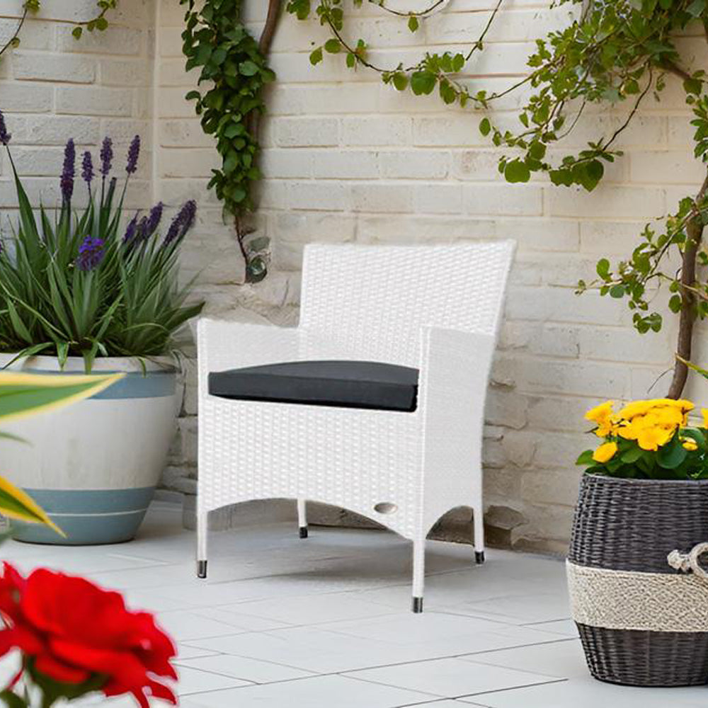 Weißer Rattanstuhl mit dunklem Sitzkissen auf Terrasse, umgeben von Blumen und Kletterpflanzen.