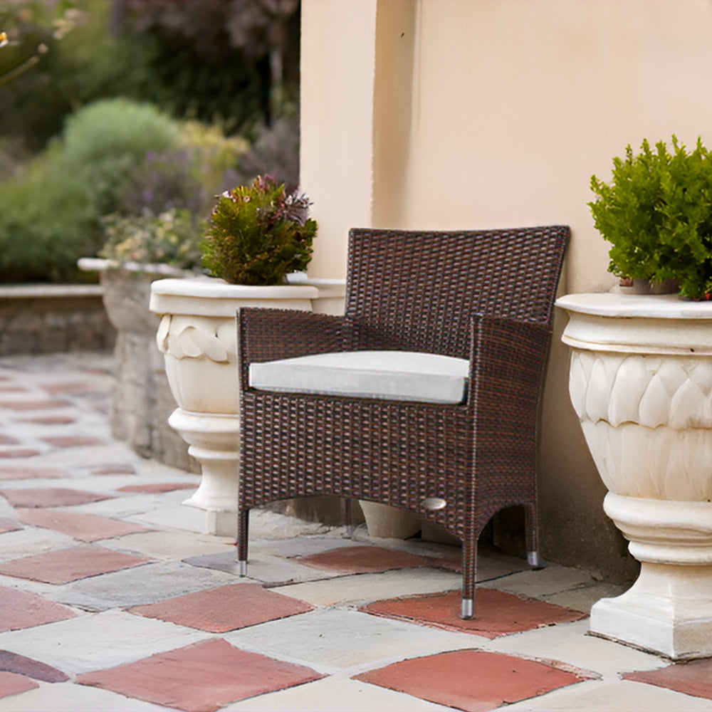 Brauner Polyrattan-Gartenstuhl mit hellem Sitzkissen zwischen zwei Blumenkübeln auf Terrasse.