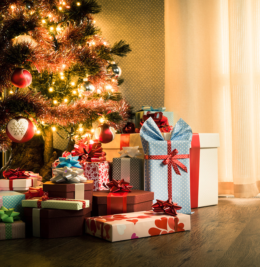 Kuenstlicher geschmückter Weihnachtsbaum mit Kugeln, Lichterkette und vielen bunt verpackten Geschenken. 210 cm