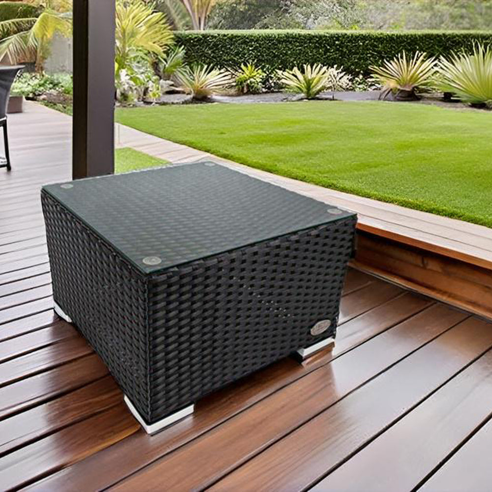 Schwarzer Rattan-Beistelltisch mit Glasplatte auf Holzterrasse, Garten im Hintergrund.
