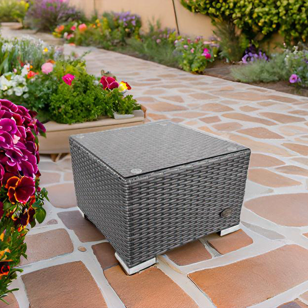 Grauer Rattan-Beistelltisch mit Glasplatte von RS Trade, platziert auf Terrasse neben bunten Blumen.