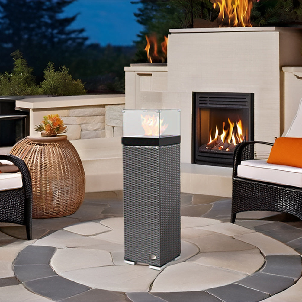 Feuersäule brennt auf Terrasse mit Kamin und Rattanmöbeln in gemütlichem Ambiente.