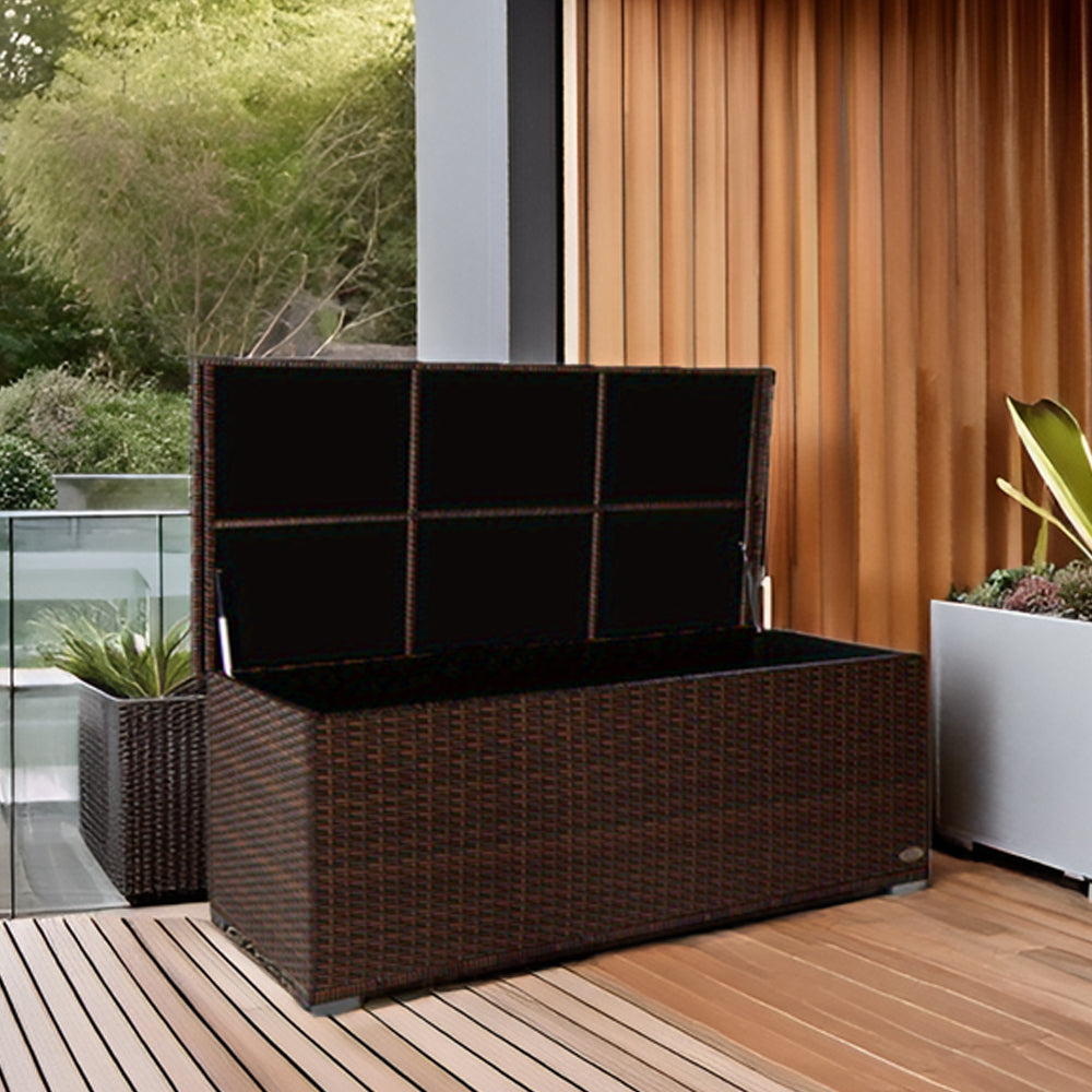 Geöffnete Aufbewahrungsbox in brauner Rattan-Optik auf einer Terrasse mit Holzbelag, daneben Pflanzen und eine Glasbrüstung.