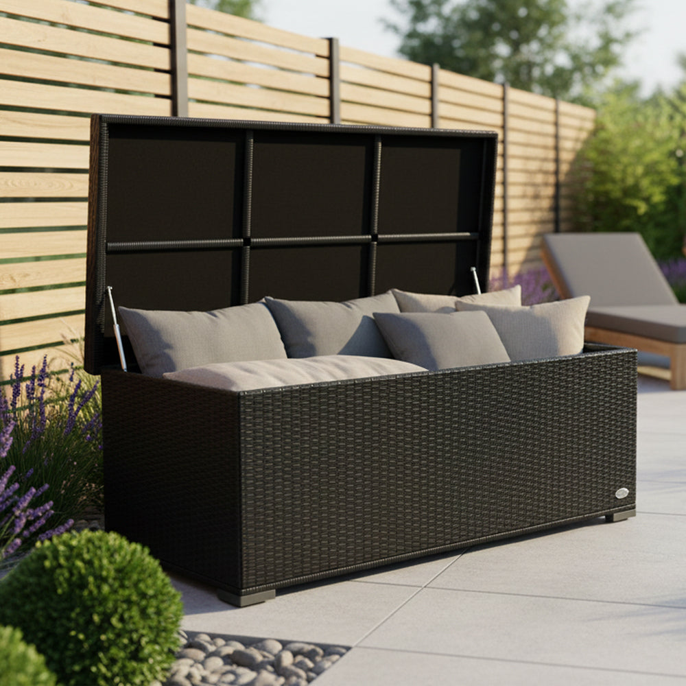 Schwarze Garten-Auflagenbox aus Polyrattan mit geöffnetem Deckel und grauen Kissen auf einer Terrasse vor Holzzaun.