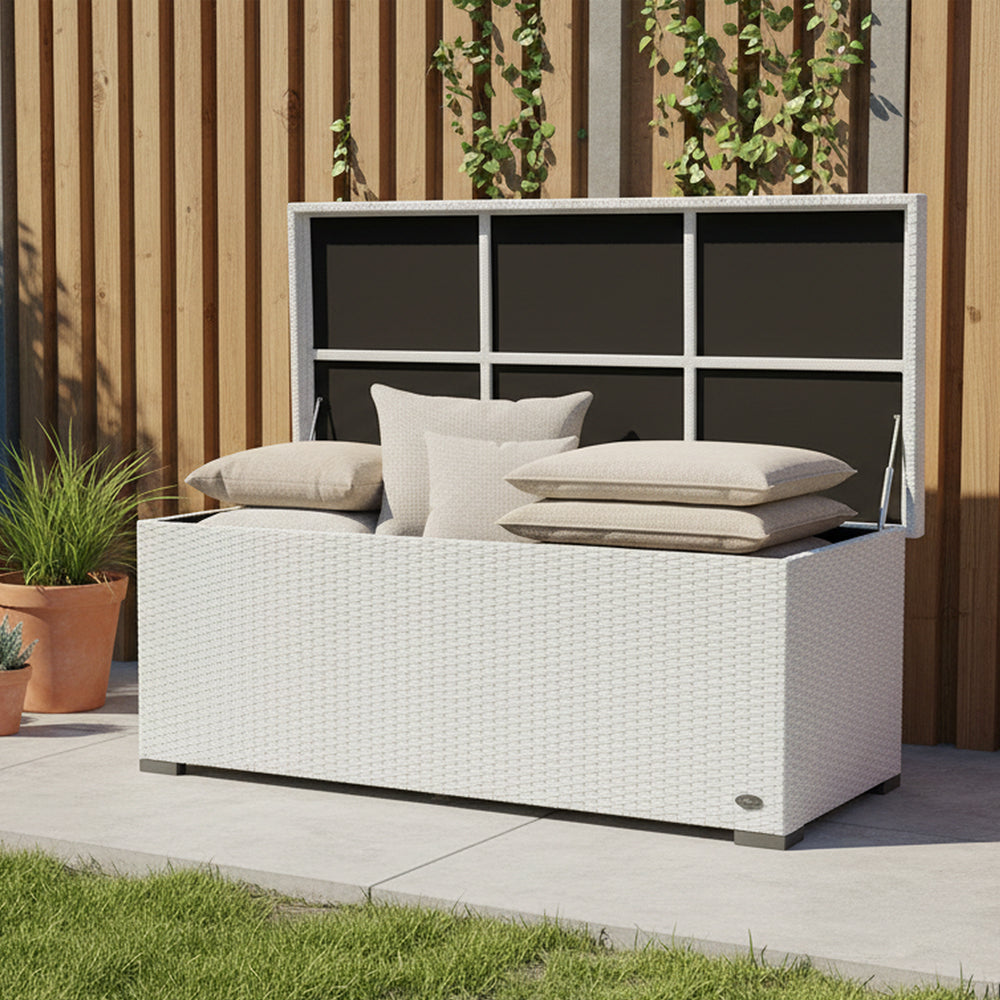 Gartenbox aus weißem Rattan mit geöffnetem Deckel auf heller Terrasse, umgeben von Pflanzen.