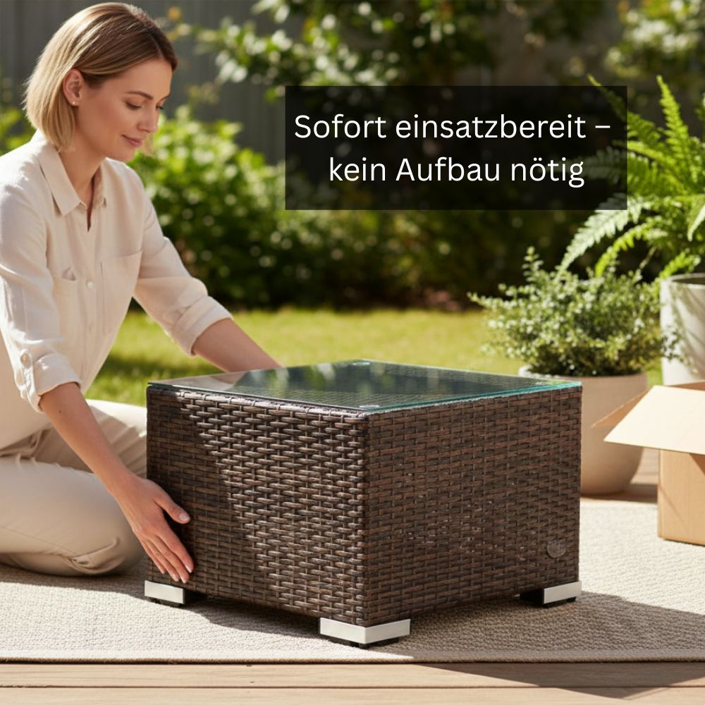 Brauner Polyrattan-Beistelltisch mit Glasplatte auf einer Terrasse. Eine Person positioniert den vormontierten Tisch neben einer geöffneten Versandverpackung.