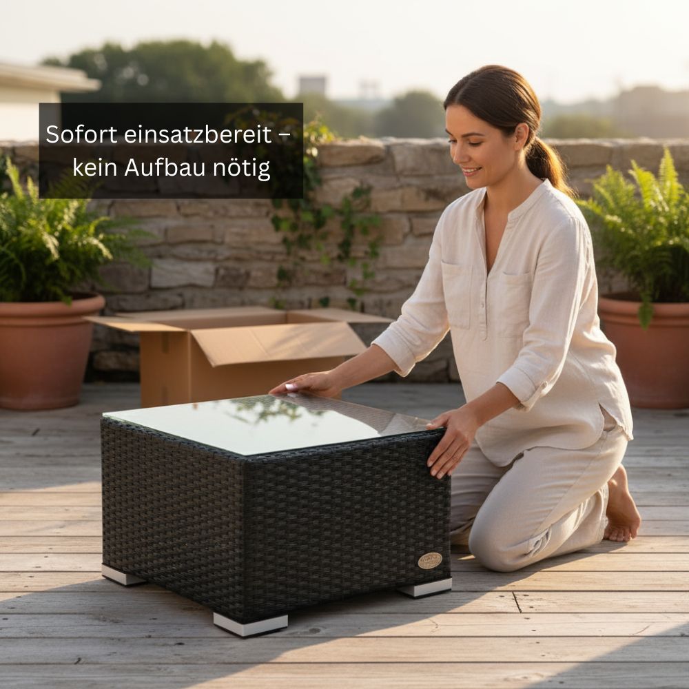 Schwarzer Polyrattan-Beistelltisch mit Glasplatte auf einer Terrasse. Eine Person positioniert den vormontierten Tisch neben einer Versandverpackung.
