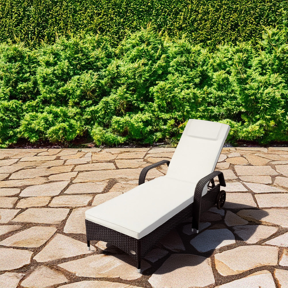 Schwarzer Rattan-Liegestuhl mit Polster steht auf einer Terasse und grünen Pflanzen.