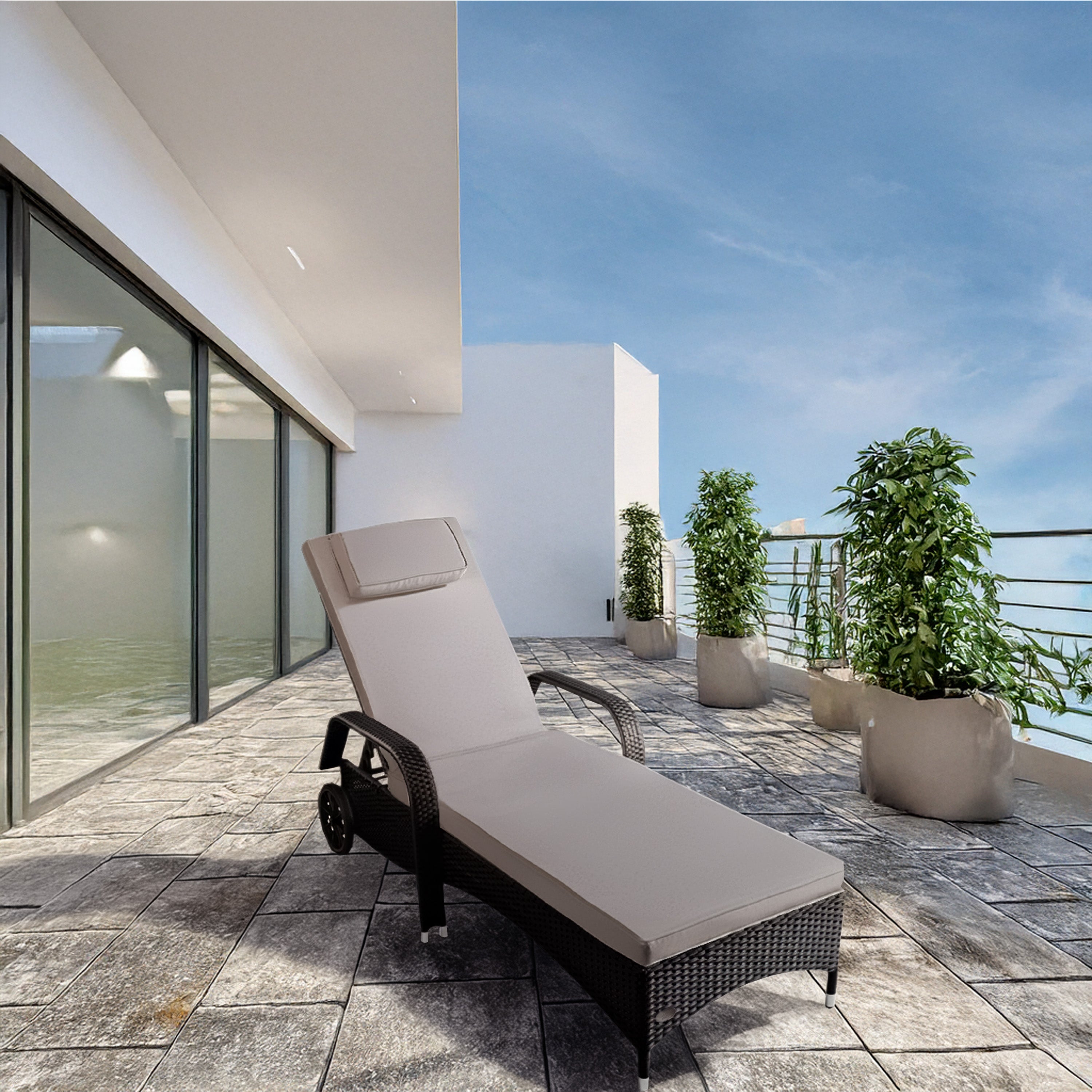 Schwarzer Rattan-Liegestuhl mit Polster steht auf einer Terasse und grünen Pflanzen.