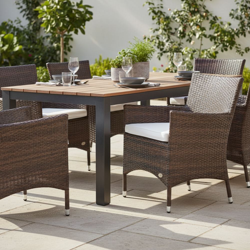 Brauner Polyrattan-Gartenstuhl „Trento“ mit hellem Sitzkissen an modernem Esstisch auf sonniger Terrasse. Wetterfester Outdoor-Stuhl mit Armlehnen für Garten, Balkon und Terrasse.