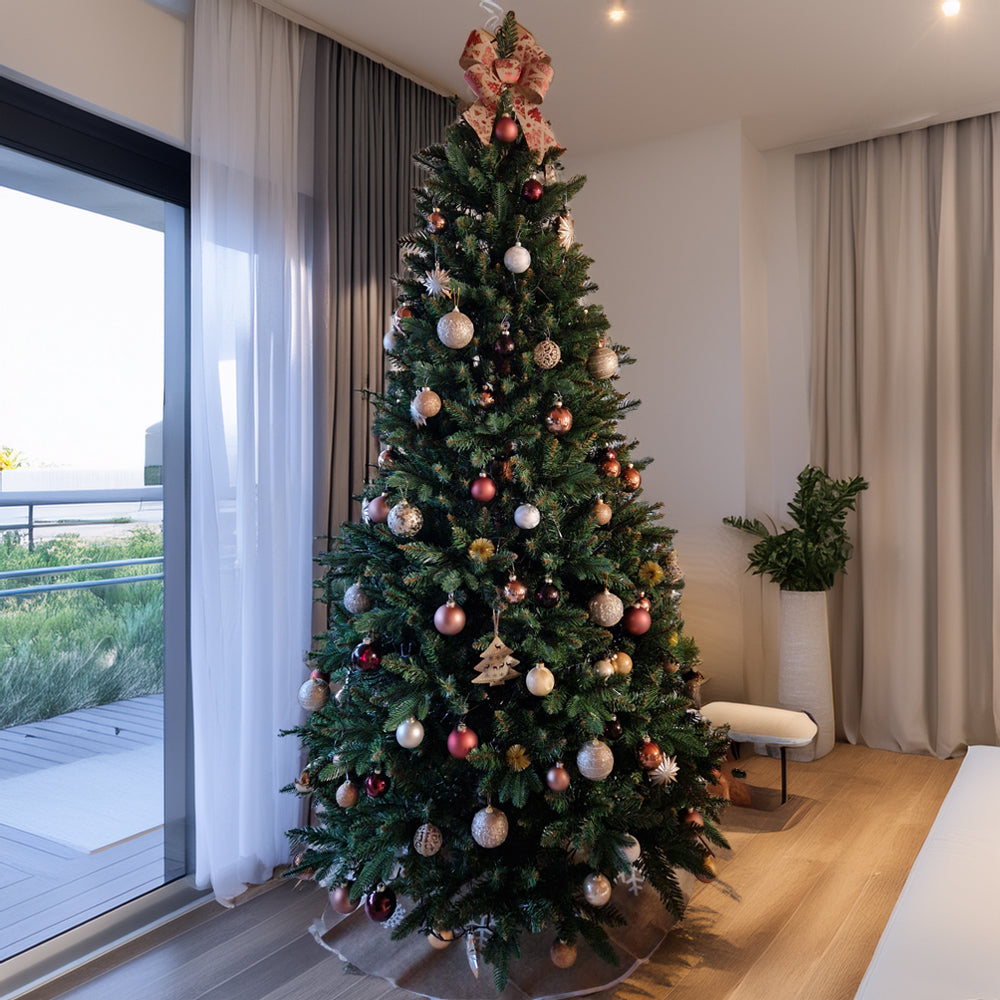 Weihnachtsbaum mit goldenen und roten Kugeln sowie Schleife an der Spitze, in modernem Wohnzimmer.