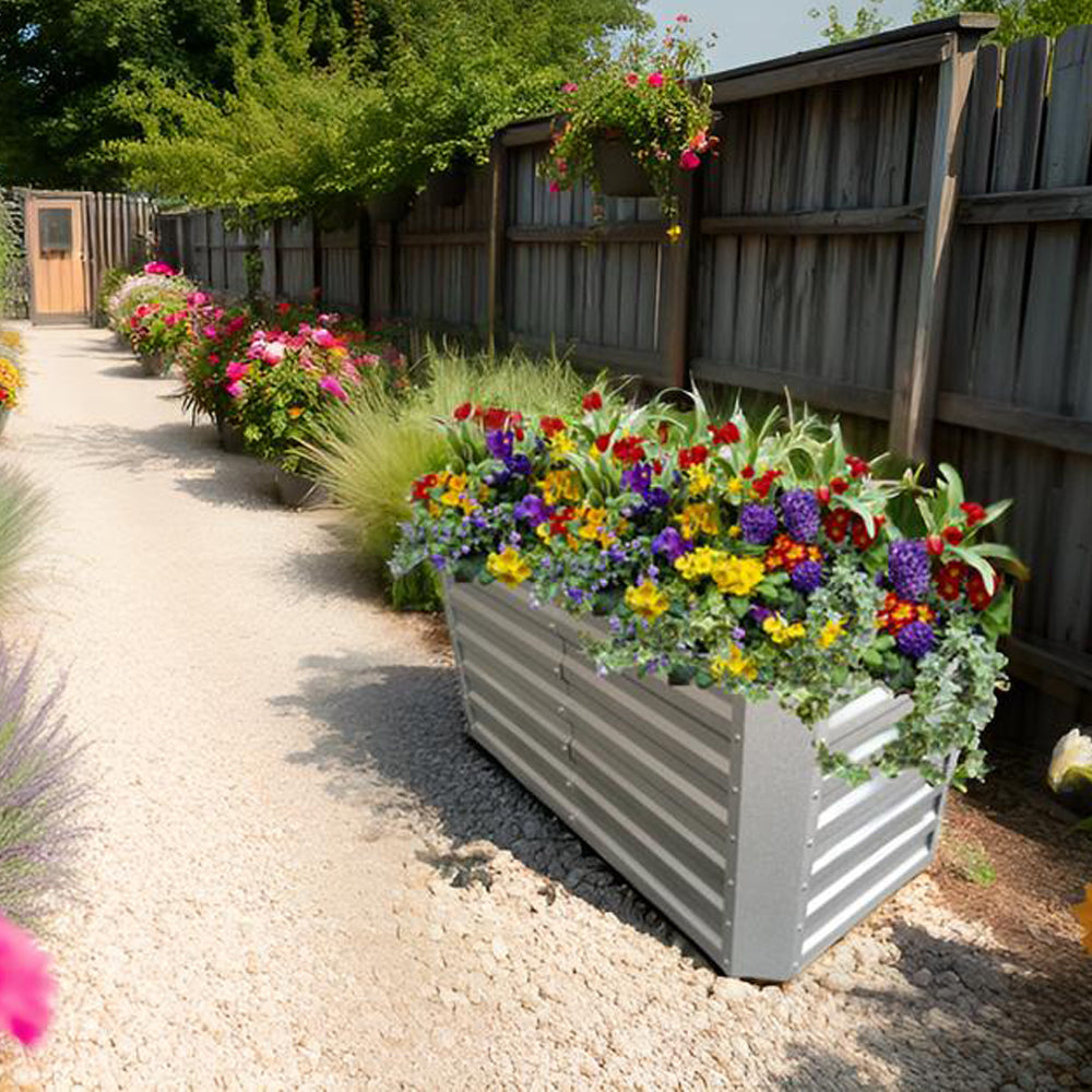 Metall-Hochbeet mit bunten Blumen, auf Kiesweg neben Holzzaun und Beeten platziert.1