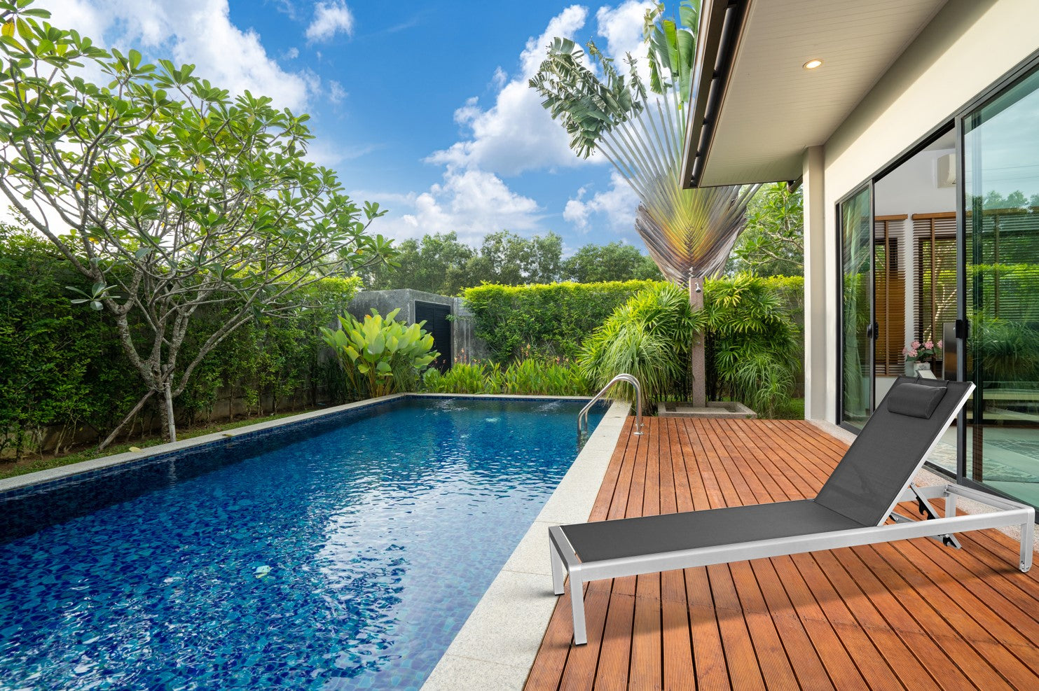 Ein moderner Gartenstuhl steht auf einer Holzterrasse am Pool mit grünem Garten im Hintergrund.