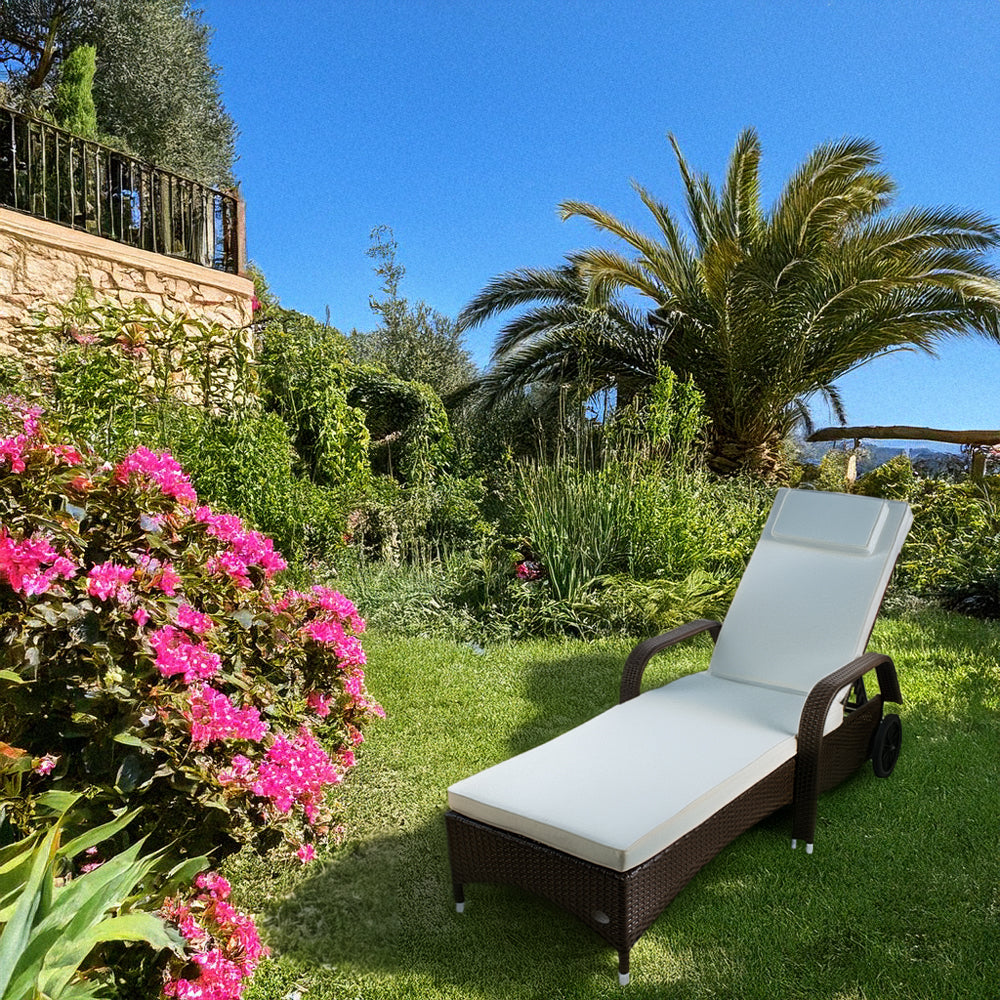 Brauner Rattan-Liegestuhl mit Polster steht in einem Garten mit schönen grünen Pflanzen.