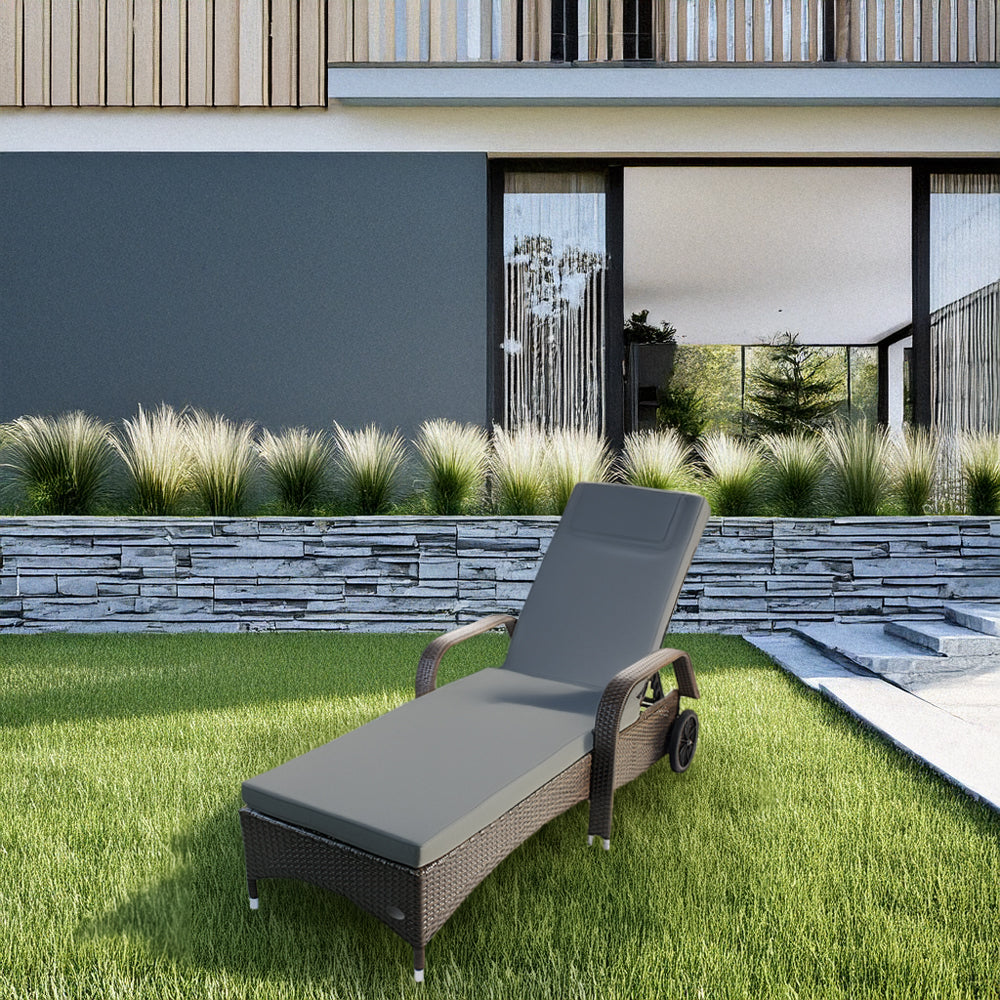 Brauner Rattan-Liegestuhl mit Polster steht in einem Garten.