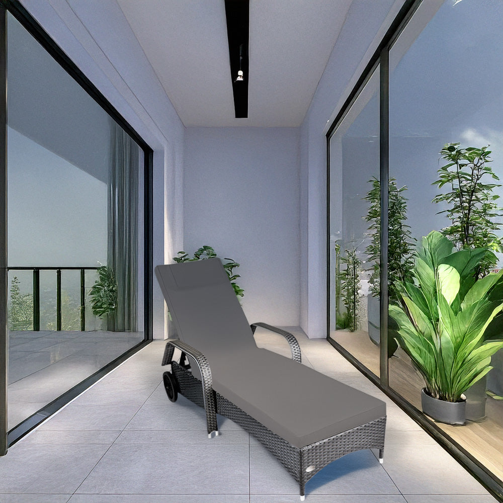 Grauer Rattan-Liegestuhl mit Polster steht in einem hellen Raum mit Glaswänden und grünen Pflanzen.