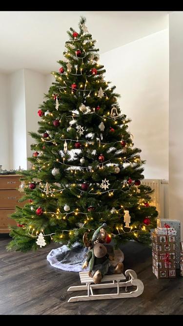 Festlich geschmückter Weihnachtsbaum mit Lichterkette, roten Kugeln und Holzanhängern im Wohnzimmer.